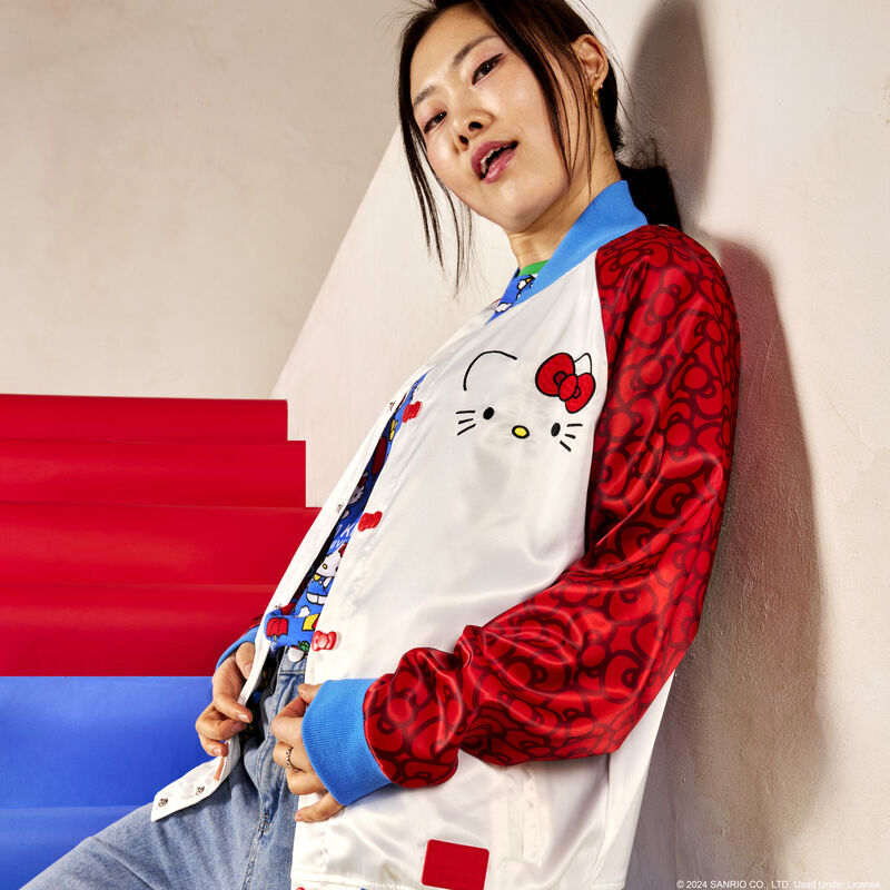 asian female modeling hello kitty 50th anniversary satin jacket posing on red & blue stairs