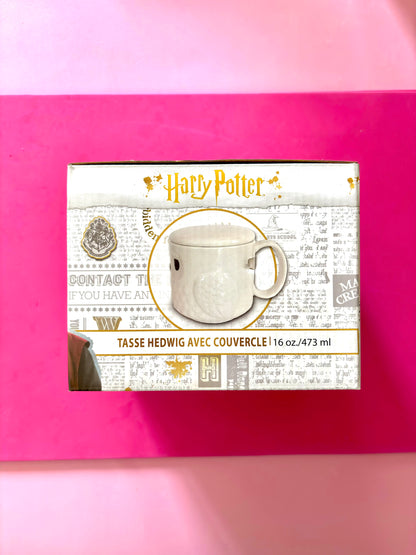 A boxed Harry Potter themed mug set on a bright pink background. The front of the package shows the Harry Potter logo, a photo of a white ceramic mug, and French text reading 'TASSE HEDWIG AVEC COUVERCLE' and '16 oz / 473 ml'.