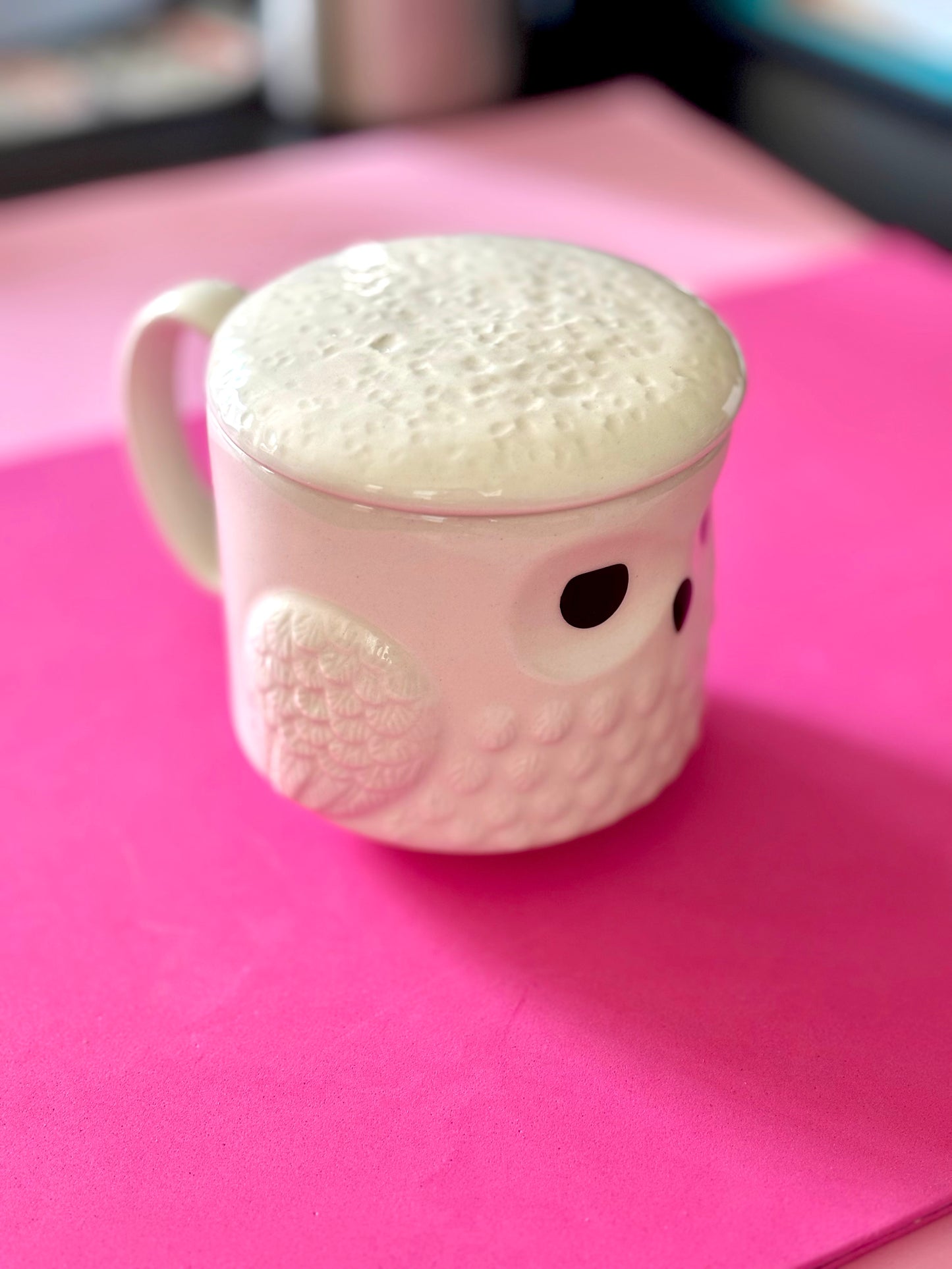 A white ceramic owl mug with a textured, bubbly white lid, resting on a bright pink surface.