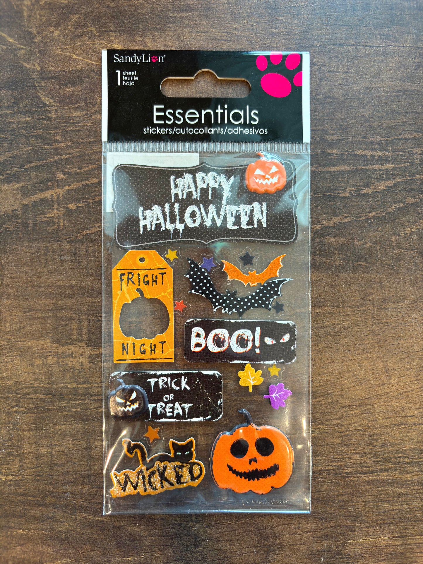 Sandy Lion Essentials Halloween sticker sheet in clear plastic packaging, featuring various spooky designs like pumpkins, bats, ghosts, and text stickers, displayed on a dark wood background.