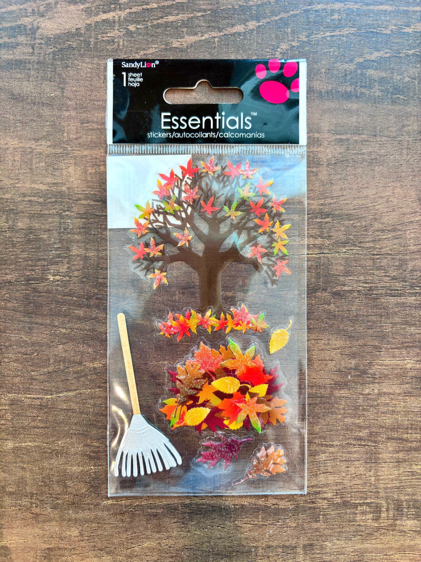 SandyLion Essentials sticker pack featuring autumn-themed stickers including a tree with colorful leaves, scattered fall leaves, and a small rake, packaged in clear plastic on a wooden surface.