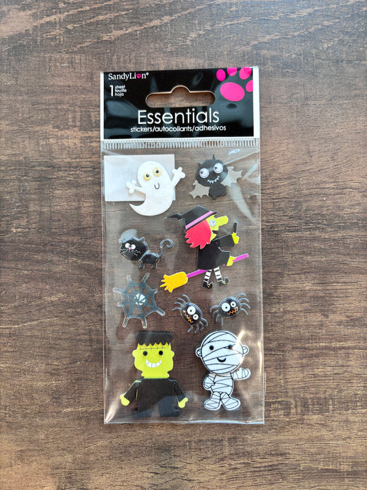 Sandy Lion Essentials Halloween-themed adhesive patch pack containing 11 different patches, displayed on a dark wood background.