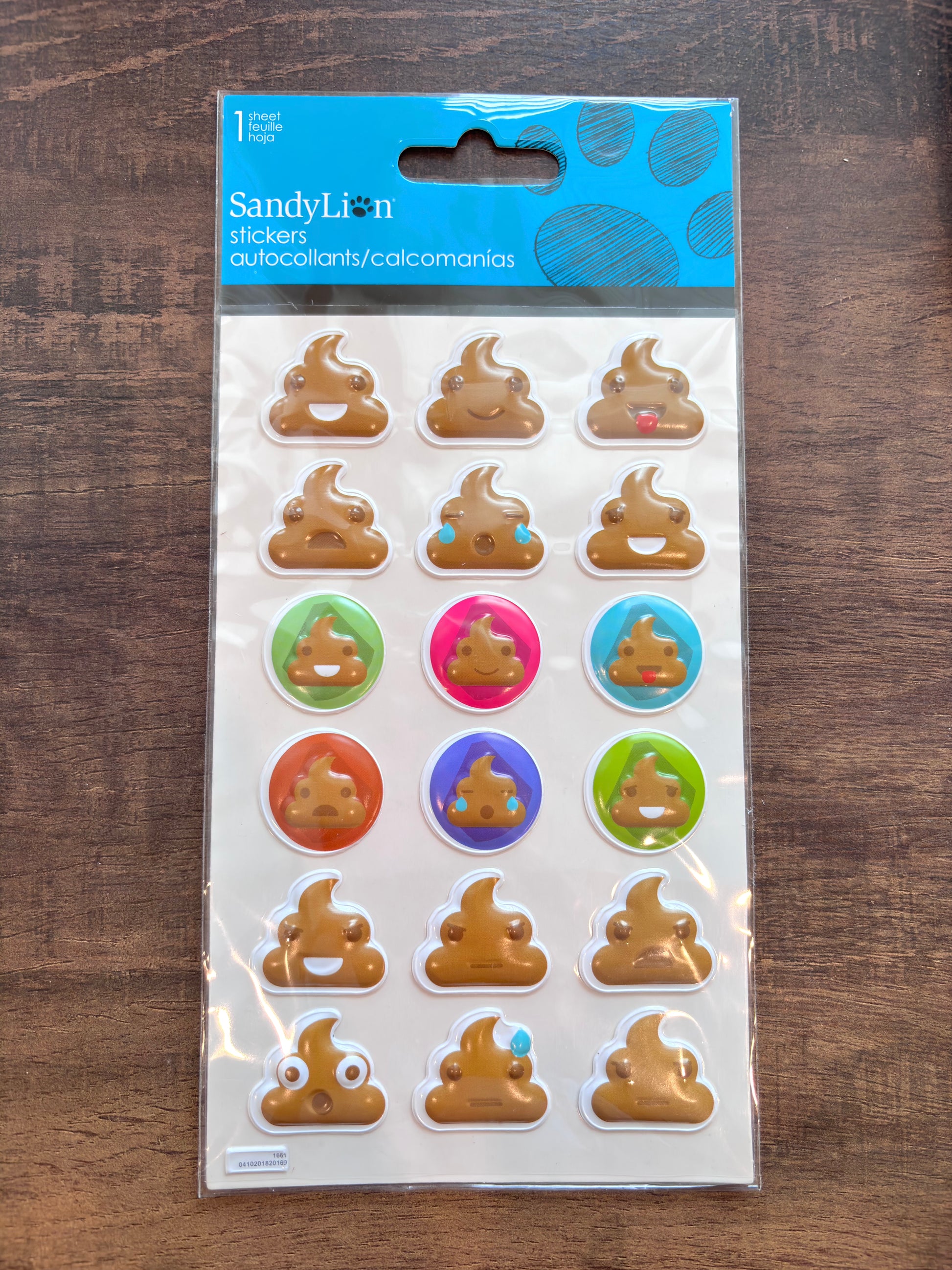 A package of Sandy Lion stickers featuring brown poop emoji designs, some with colorful accents, in its original blue and white retail packaging, placed on a dark wooden surface.