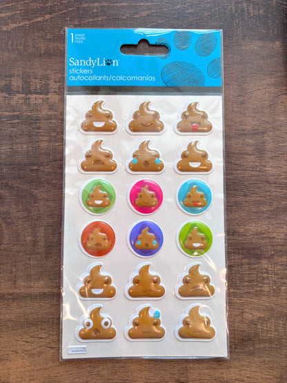 A package of Sandy Lion stickers featuring brown poop emoji designs, some with colorful accents, in its original blue and white retail packaging, placed on a dark wooden surface.