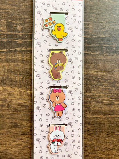 Set of four cartoon character clips on a decorative card with floral patterns, placed on a wooden surface.