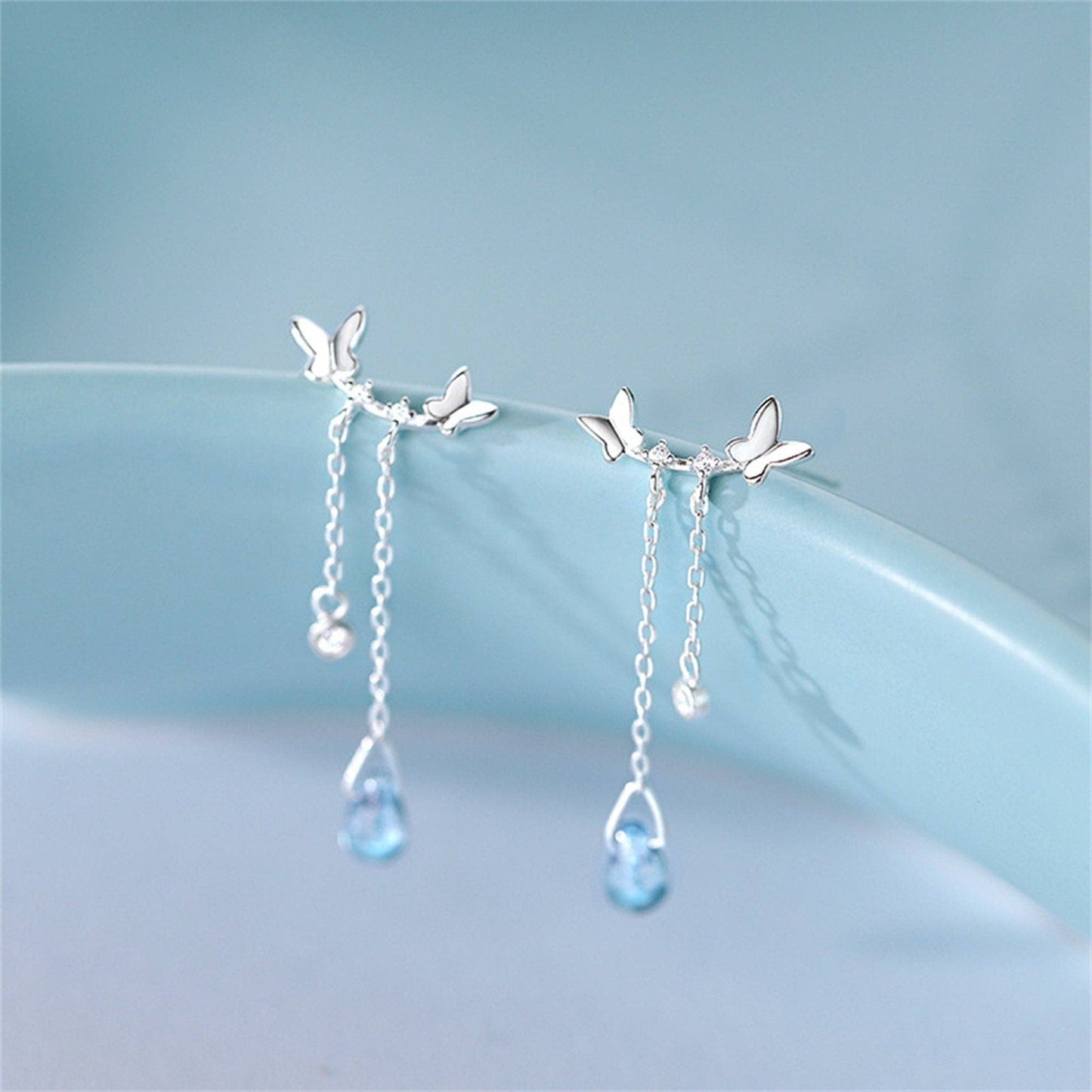 Silver earrings with butterfly designs and blue gemstones on a light blue background