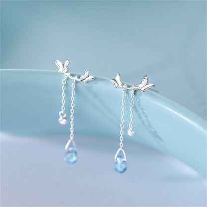 Silver earrings with butterfly designs and blue gemstones on a light blue background