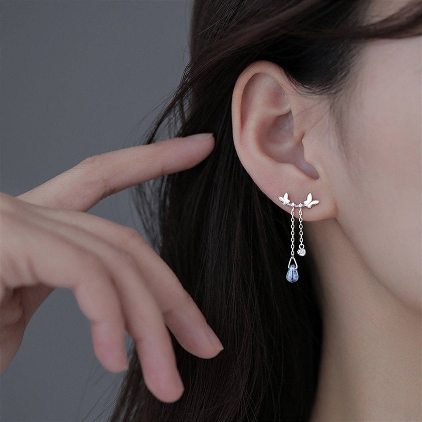 Earring worn by a person with a hand pointing to it, on a dark background