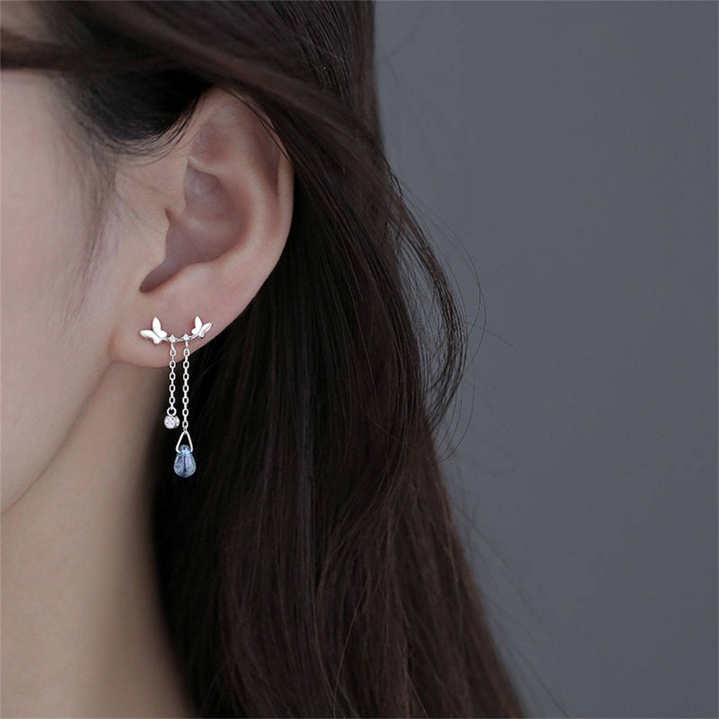 Close-up of an ear wearing a delicate earring with a gray background