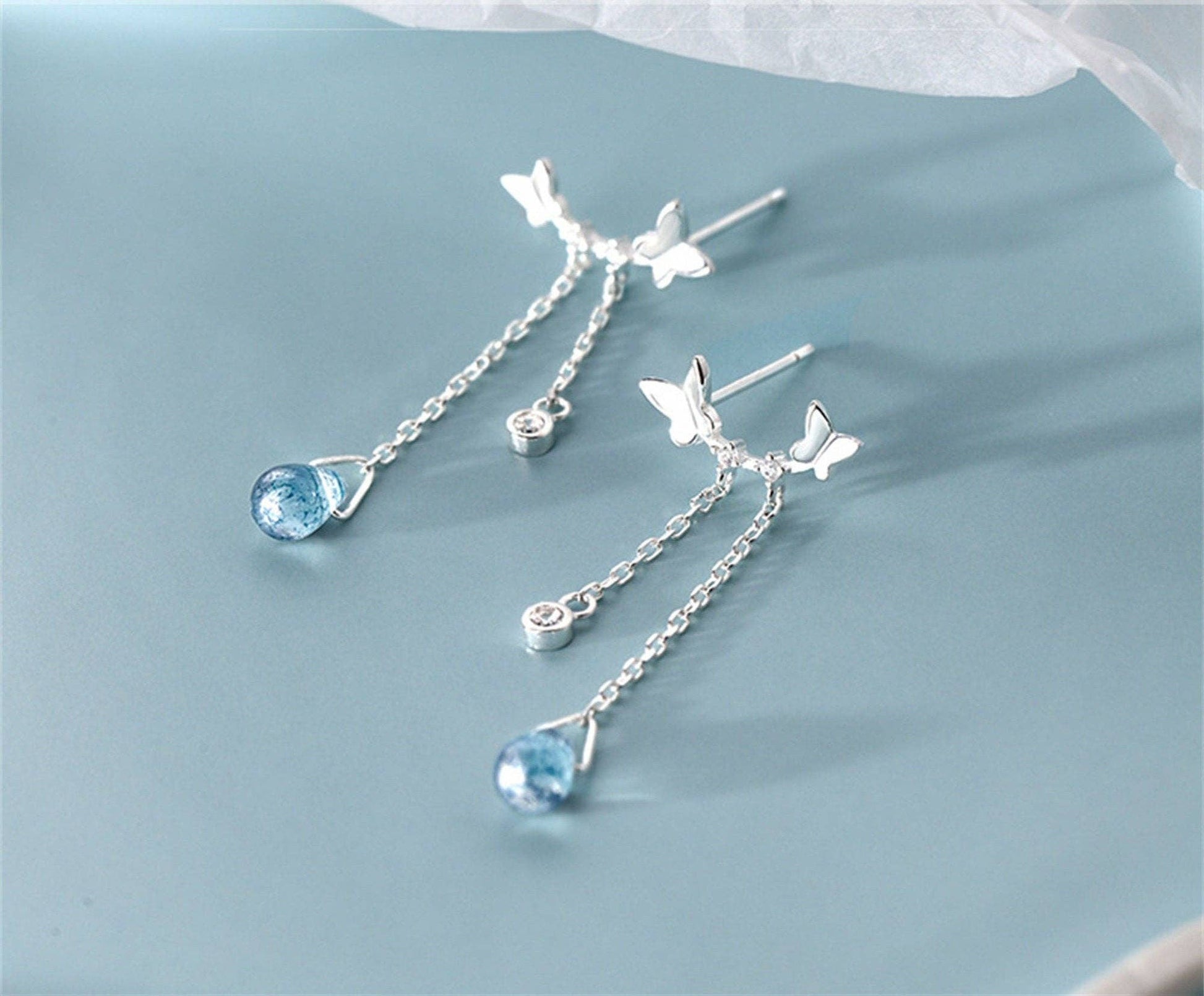 Silver earrings with blue gemstones and butterfly designs on a light blue background