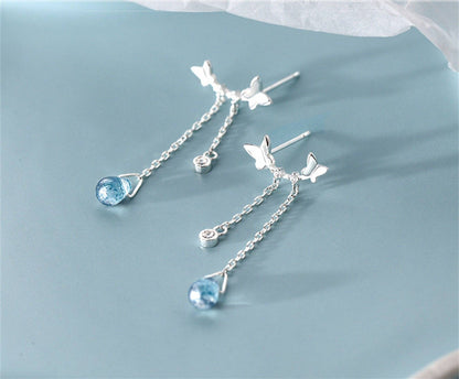 Silver earrings with blue gemstones and butterfly designs on a light blue background