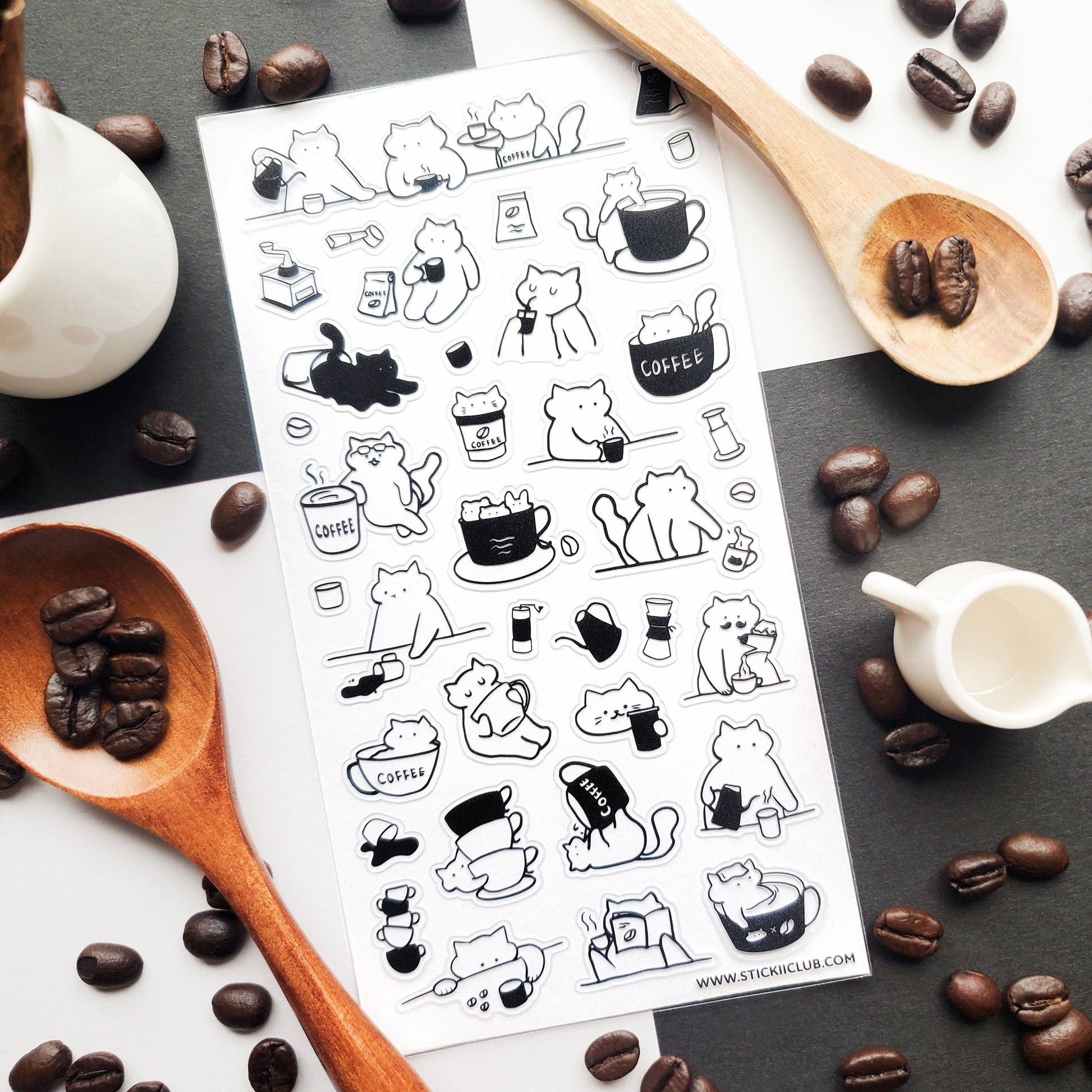 Sheet of black and white cat-themed coffee stickers on a surface with coffee beans and a wooden spoon.