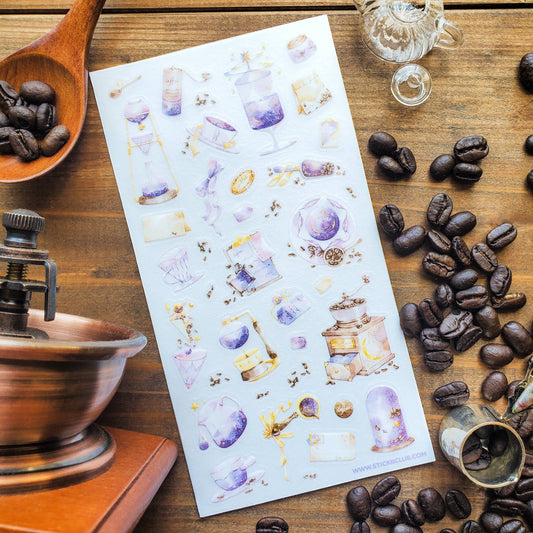 Sheet of decorative stickers with coffee-themed designs on a wooden surface with coffee beans and a grinder.