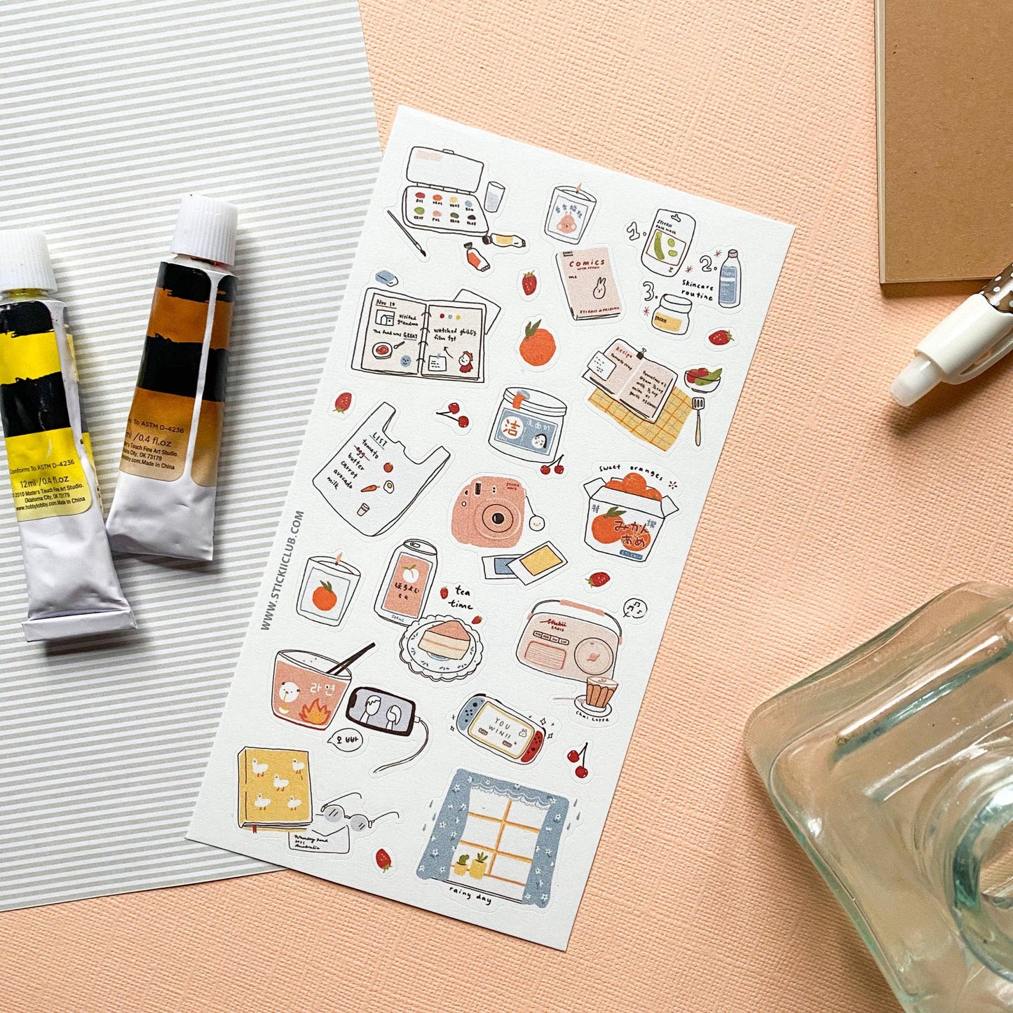 Sheet of illustrated stickers on a pink surface with art supplies.