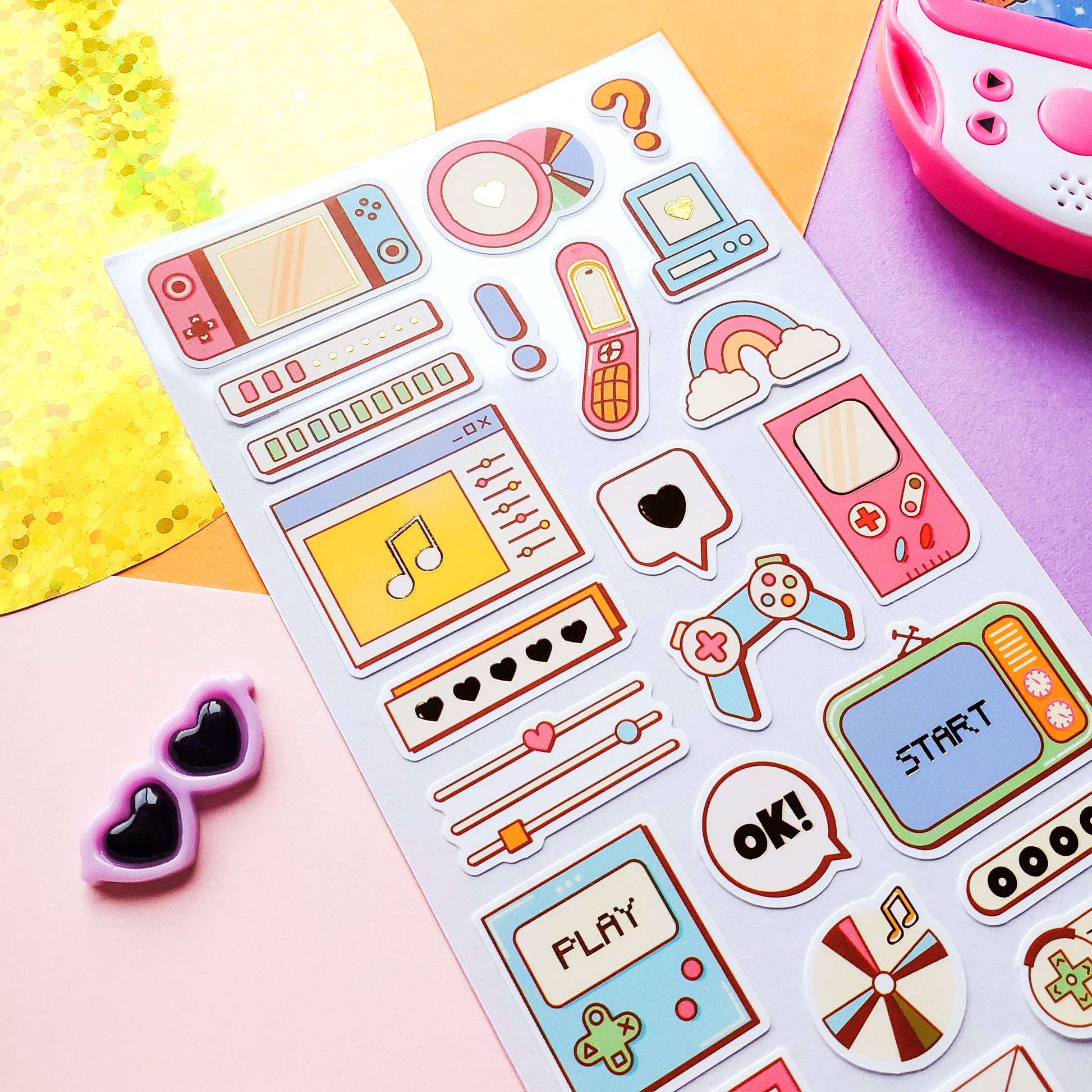 Sheet of colorful retro-themed stickers on a pink surface with sunglasses and a toy.