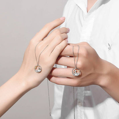 Two hands holding silver necklaces with circular pendants against a neutral background