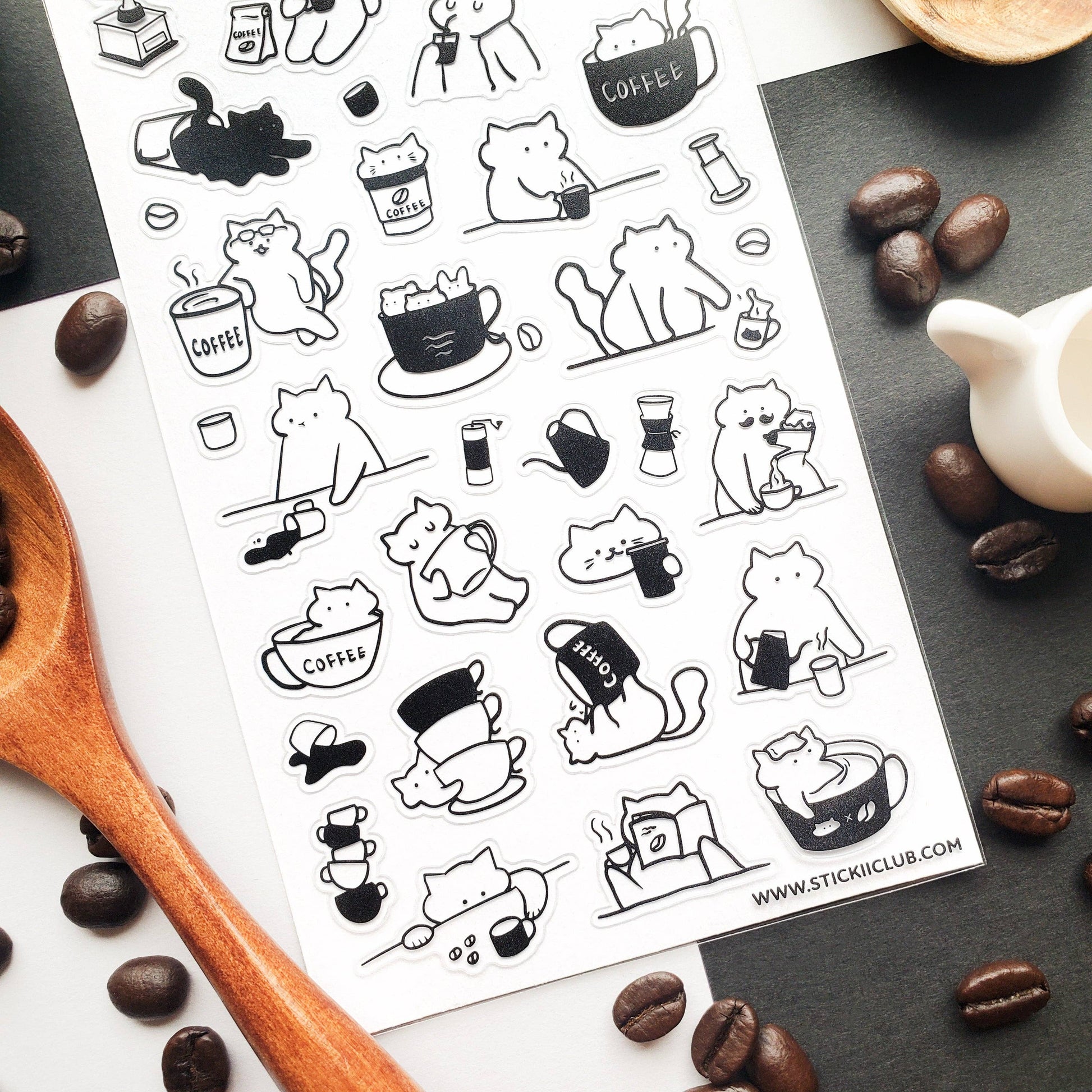 Sheet of black and white cat-themed stickers with coffee cups on a surface with coffee beans and a teapot.