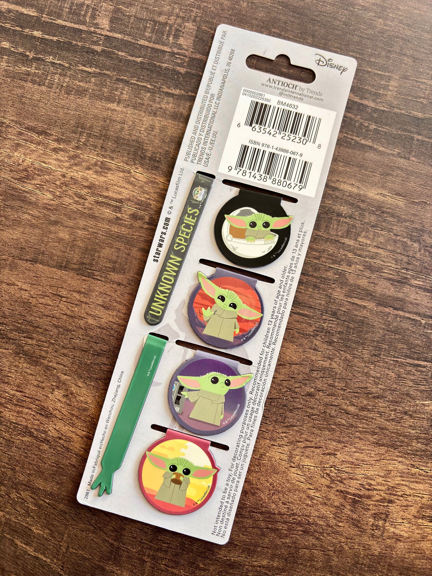 Set of four 'Baby Yoda' themed pins on a Disney packaging with a wooden surface background.