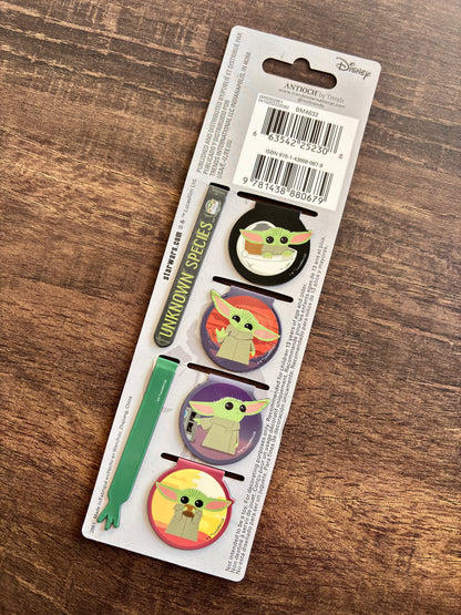 Set of four 'Baby Yoda' themed pins on a Disney packaging with a wooden surface background.