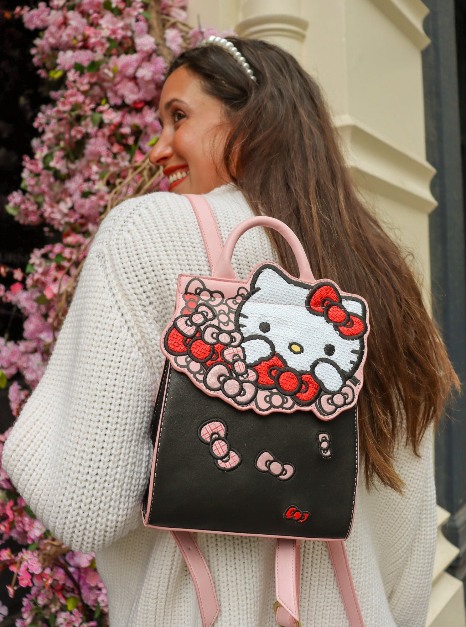 Danielle Nicole Hello Kitty black and pink bow backpack on girl's shoulder flower background